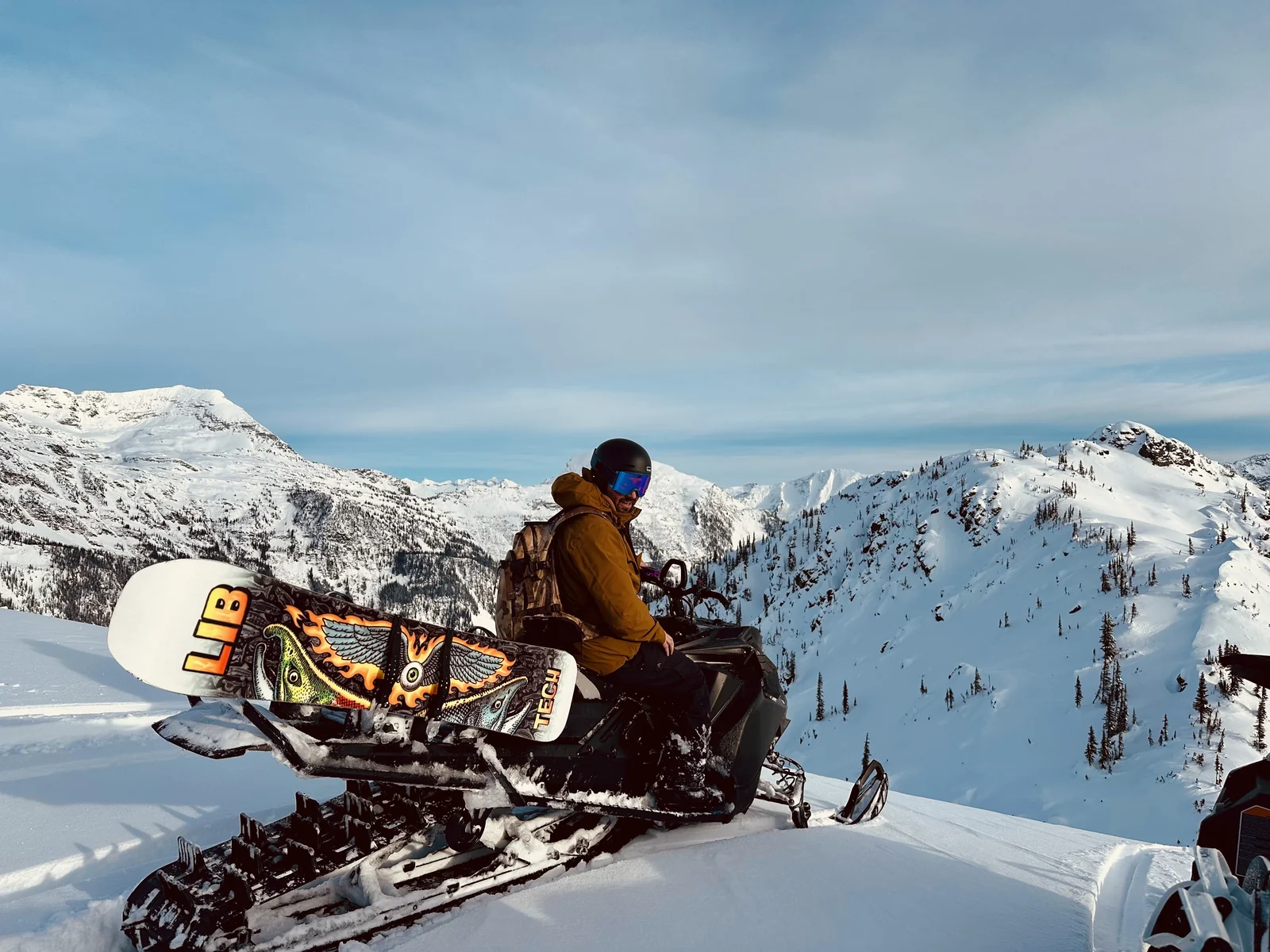 Dave Trerice on a snowmobile with his snowboard strapped on