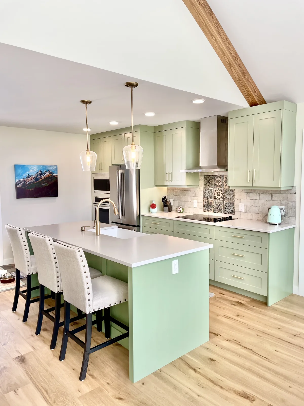 Sage green kitchen with an island, brass pendants and an exposed beam