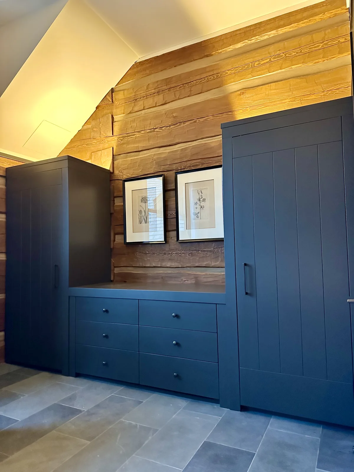 Navy built in wardrobe and drawer bank set against a log wall