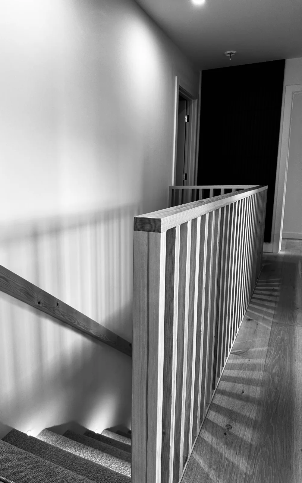 Timber stair railing in black and white, light raking across the spindles
