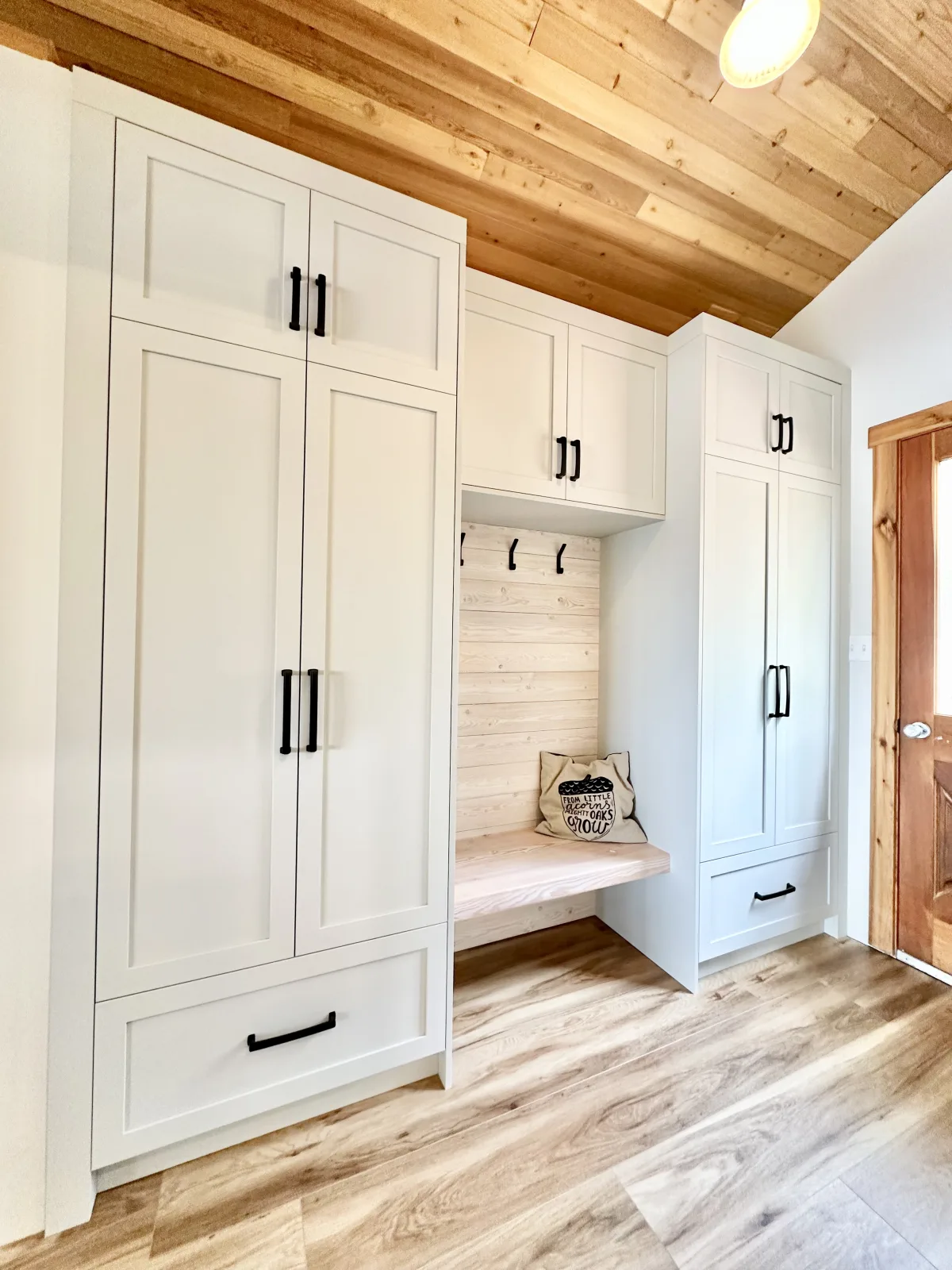 White mudroom lockers and a bench under a pine plank ceiling