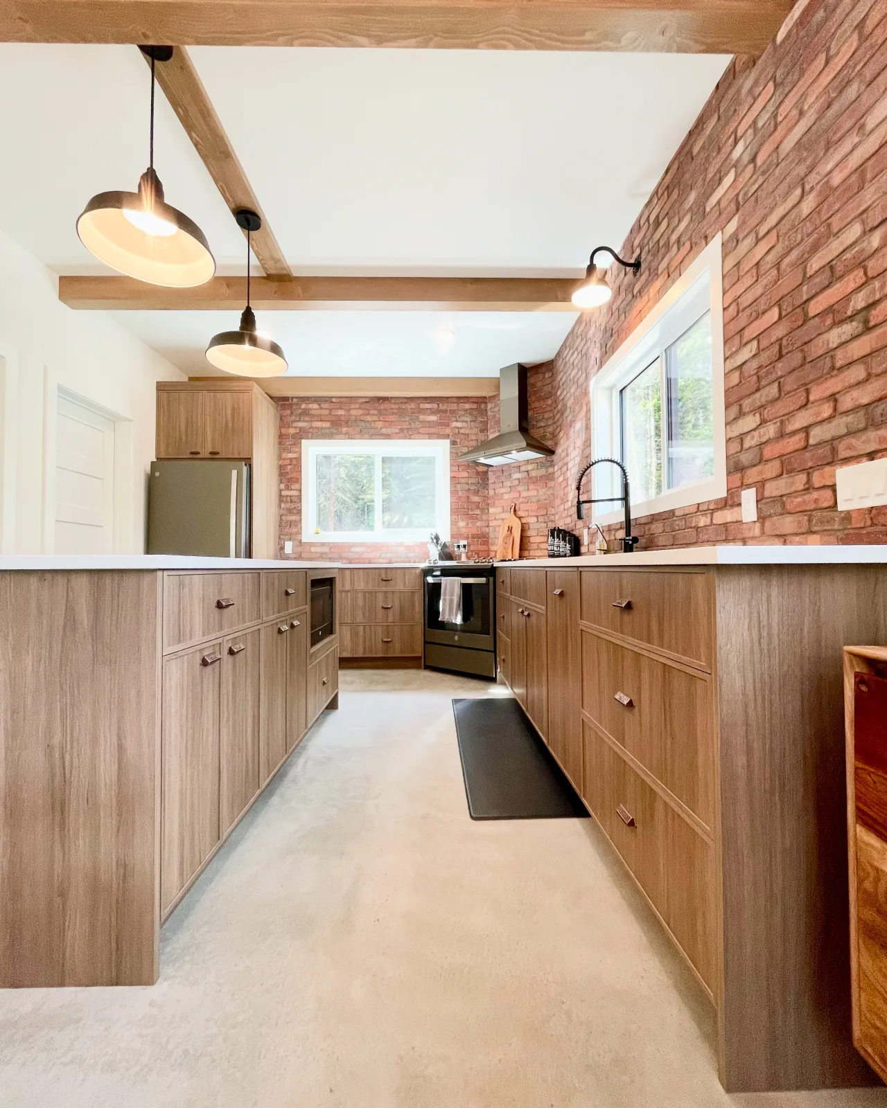 Galley kitchen in walnut toned cabinetry against an exposed brick wall