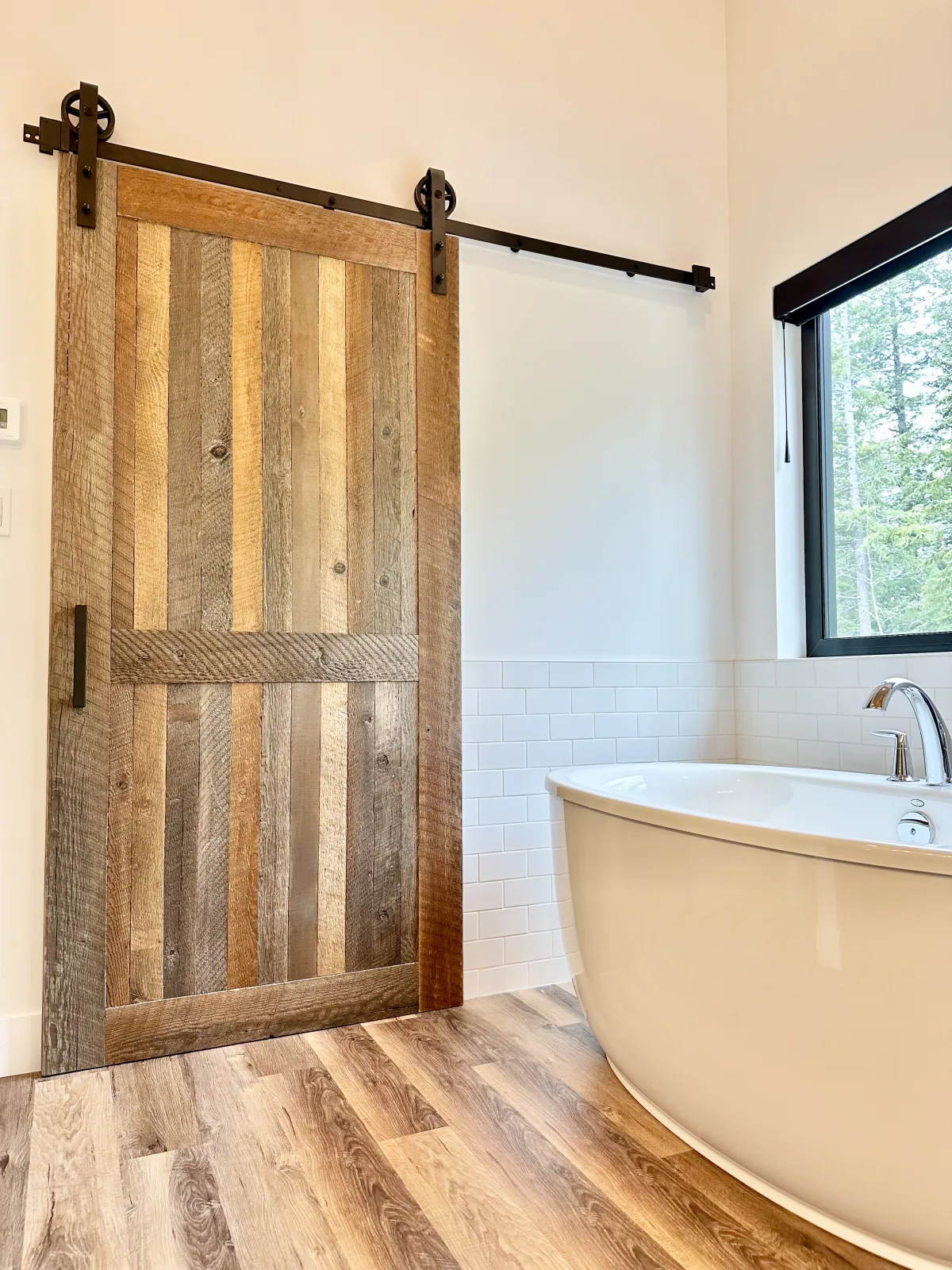 Reclaimed barnboard sliding door beside a freestanding tub in a shoreline bathroom