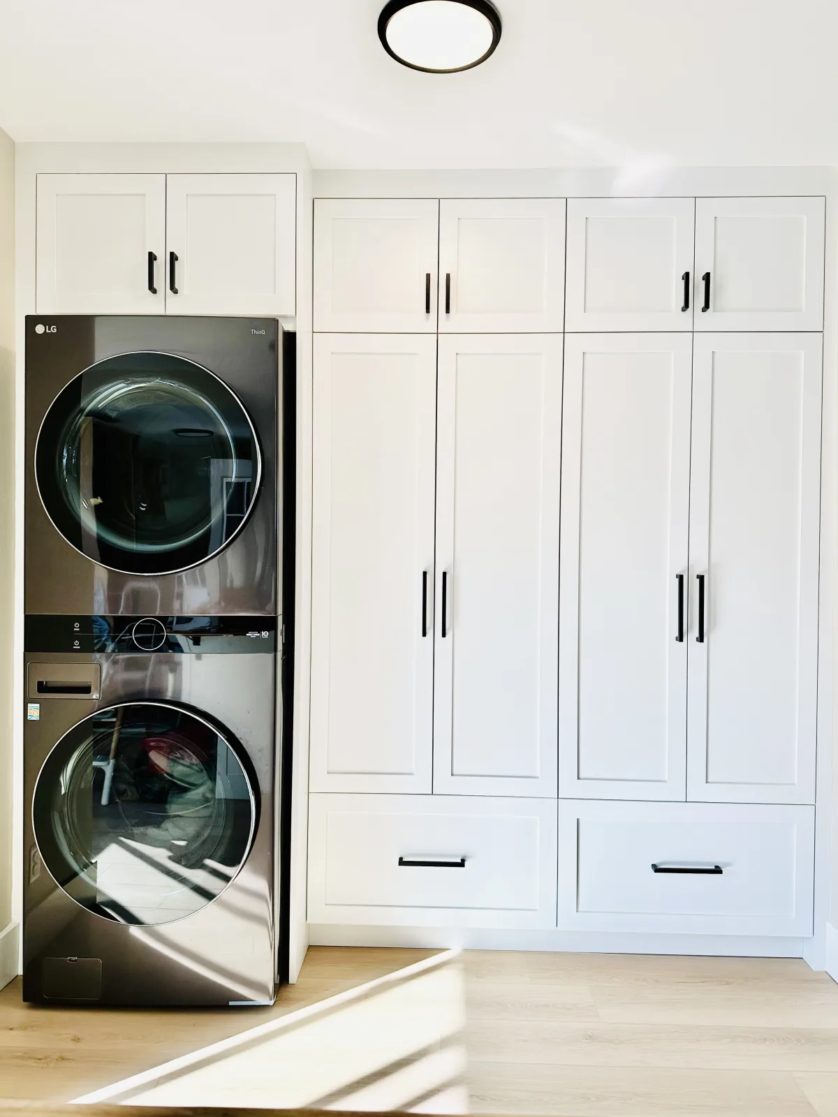 Floor to ceiling white laundry cabinetry flanking a stacked washer and dryer